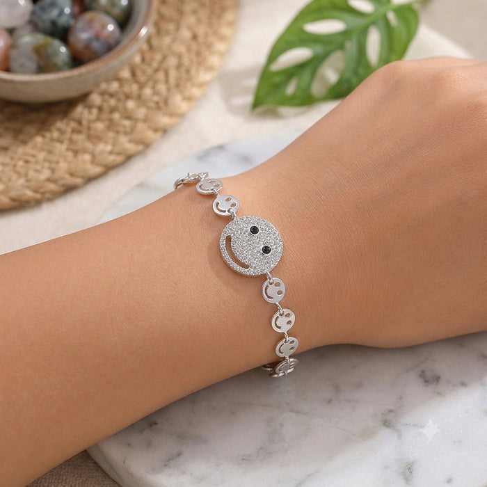 Silver bracelet with smiley face design on a wrist, marble surface with leaf and bowl in background