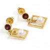 A pair of gold drop earrings featuring a round dark red gemstone and a white pearl set within a square frame, shown on a clean white background.