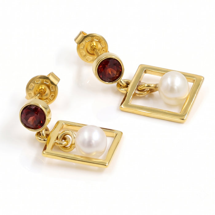 A pair of gold drop earrings featuring a round dark red gemstone and a white pearl set within a square frame, shown on a clean white background.