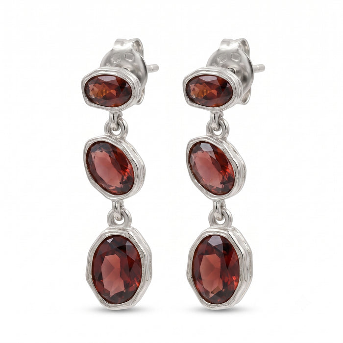 A pair of silver drop earrings featuring three faceted oval garnet stones in each earring, set in textured silver bezels on a plain white background.