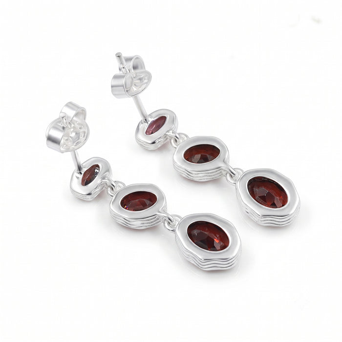 A pair of silver drop earrings featuring three oval-cut dark red gemstones in each earring, set in a wavy, layered silver bezel design with secure post-back closures, shown on a plain white background.
