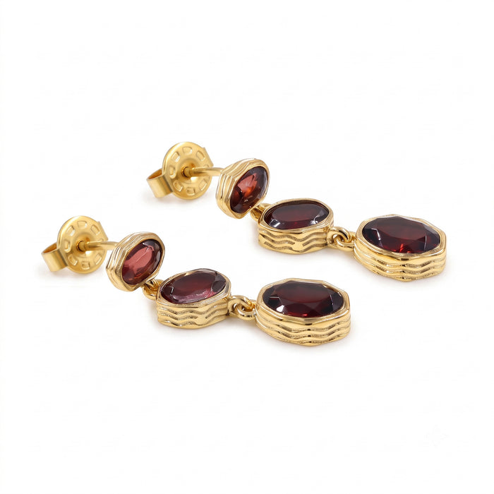 A pair of gold drop earrings with oval dark red garnet gemstones, shown on a clean white background.