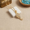A gold seahorse pendant necklace adorned with small clear stones, displayed on a white marble block over a beige linen surface with a wooden bowl in the background.