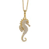 A gold seahorse pendant necklace paved with small clear stones, hanging from a gold chain against a plain white background.