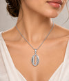 A close-up of a woman wearing a silver pendant necklace with a bohemian shell design featuring a central chain-link cutout.
