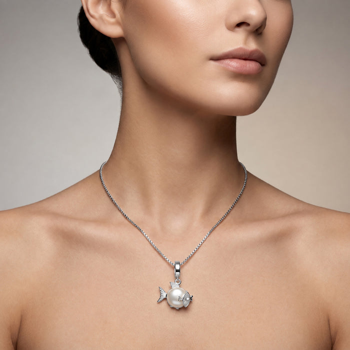 A close-up of a woman's neck and upper chest wearing a silver chain necklace with a fish-shaped pendant featuring a white pearl.