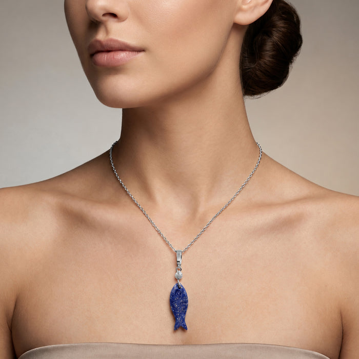 A close-up of a model wearing a silver chain necklace with a blue fish pendant, set against a neutral beige background.