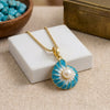 A gold chain necklace with a nautilus shell pendant featuring a central pearl, displayed on a white jewelry box over a beige fabric surface.