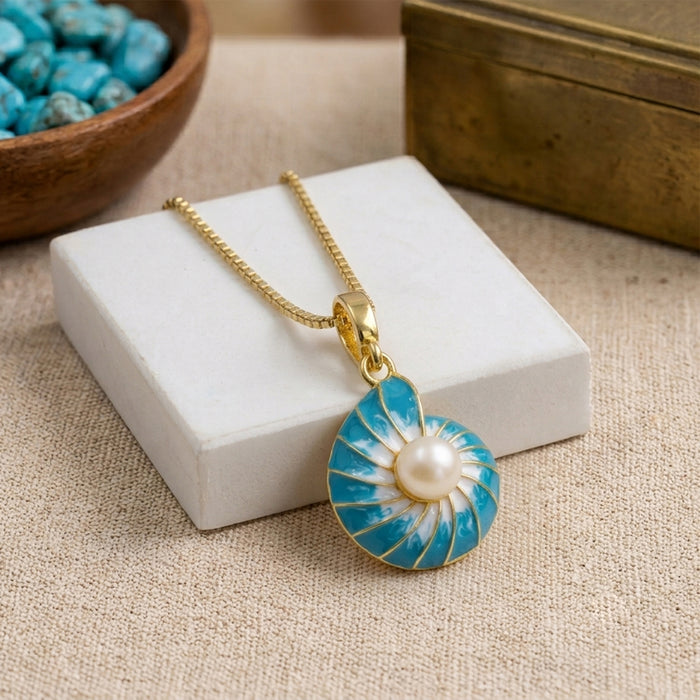 A gold chain necklace with a nautilus shell pendant featuring a central pearl, displayed on a white jewelry box over a beige fabric surface.