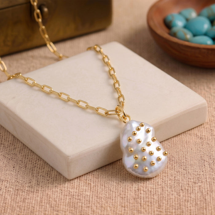 Close-up view of a baroque freshwater pearl pendant showing the textured metallic stud details and gold bail
