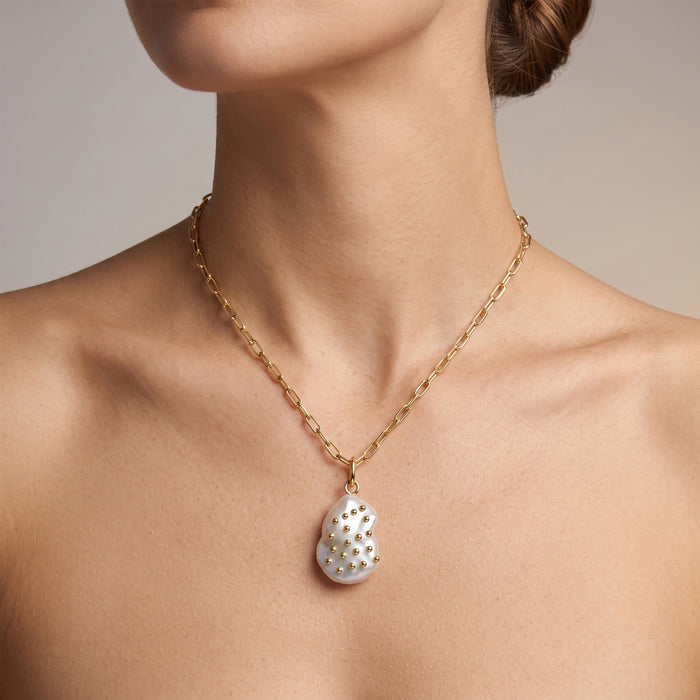 Model wearing a gold paperclip chain necklace with a baroque freshwater pearl pendant layered against a black top