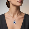 A close-up of a woman wearing a silver-toned necklace with a circular pendant featuring a deep blue oval  lapis lazuli center stone and small clear stones around it.
