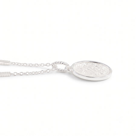 A silver oval pendant necklace with a textured, hammered finish inside a polished bezel setting, suspended from a delicate link chain against a plain white background.