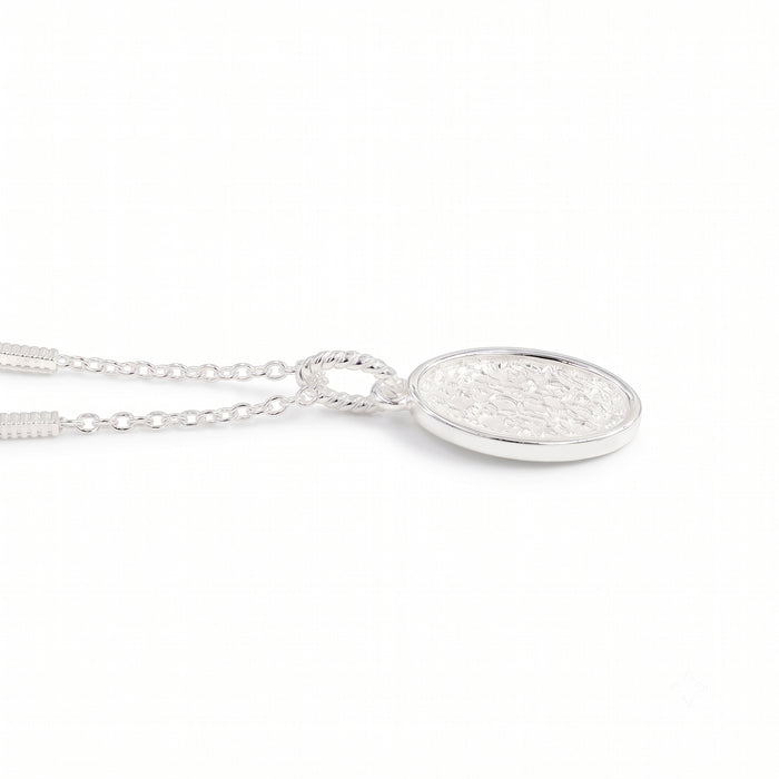 A silver oval pendant necklace with a textured, hammered finish inside a polished bezel setting, suspended from a delicate link chain against a plain white background.