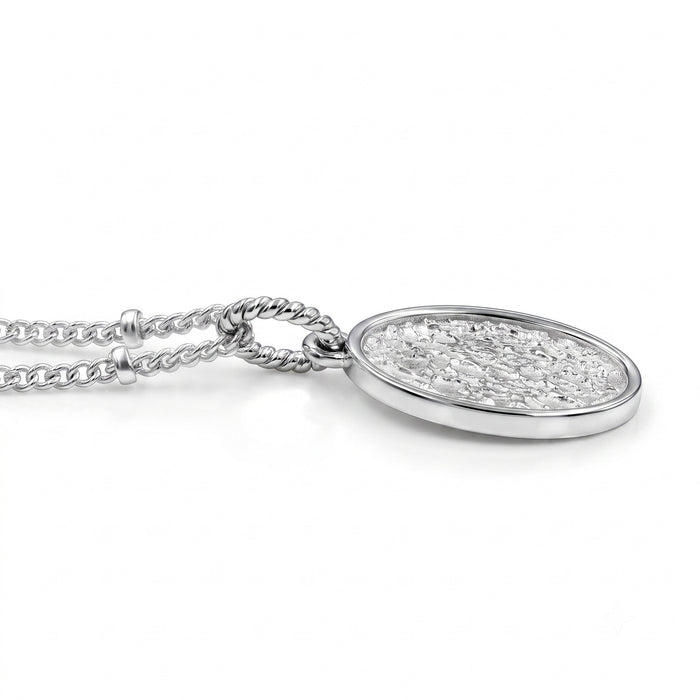 A silver oval pendant necklace with a textured, glittery silver inlay, suspended from a silver chain on a white background.