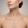 A close-up of a woman wearing a delicate silver chain necklace with a silver oval pendant set with clear stones, shown against a neutral beige background.