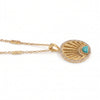 A gold pendant necklace featuring a sunburst design with a small turquoise heart-shaped stone and a border of clear pavé stones, shown on a white background.