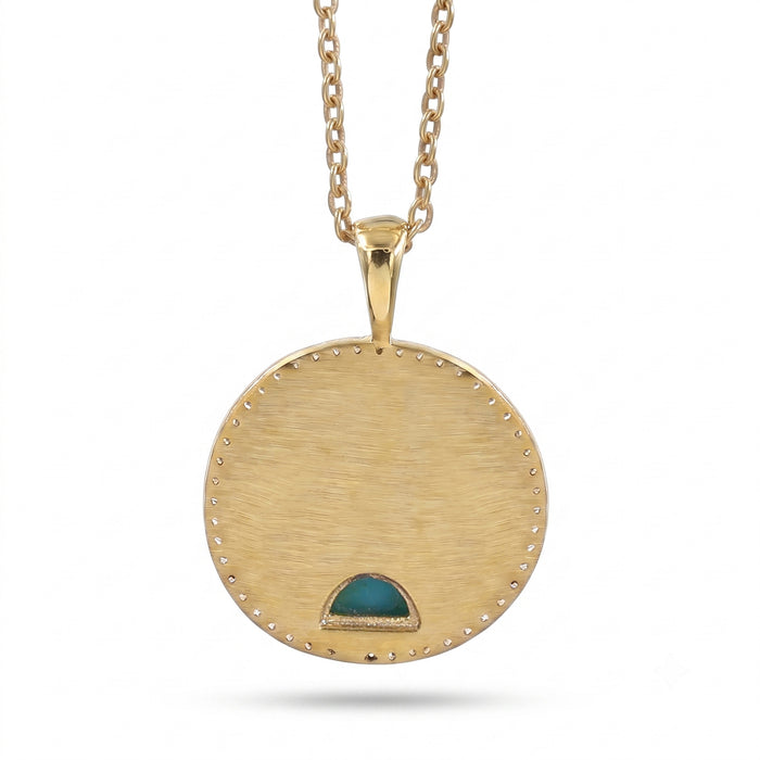 A gold round pendant necklace with a brushed finish, featuring a small green inlay at the bottom and a beaded border, suspended from a gold chain against a white background.