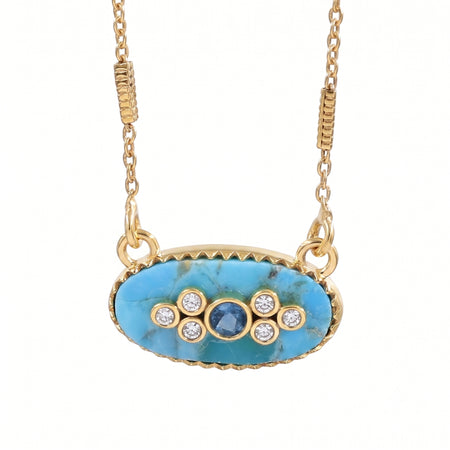 Gold oval pendant necklace featuring a turquoise-blue marbled stone center with a small round blue stone and five clear accent stones, suspended from a gold chain on a white background.