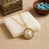 A gold-toned pendant necklace with a circular bull design and small black onyx stones around the edge, displayed on a white stone block over a beige fabric surface.