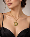 A close-up of a model wearing a gold chain necklace with a circular pendant featuring a silver bull motif and black onyx accents, styled with a black satin top against a neutral background.