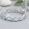 Silver ring with Aquamarine light blue stones on a gray surface with greenery in the background
