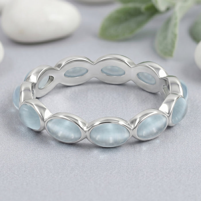 Silver ring with Aquamarine light blue stones on a gray surface with greenery in the background