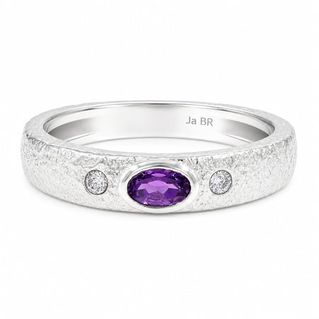 A silver band ring featuring a textured finish, a central oval purple amethyst stone, and two small round-cut clear stones on either side.