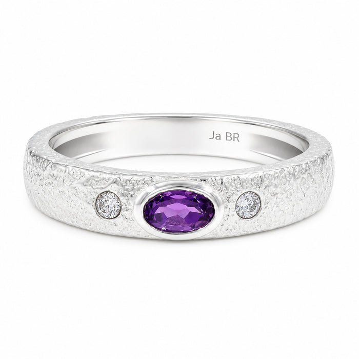 A silver band ring featuring a textured finish, a central oval purple amethyst stone, and two small round-cut clear stones on either side.