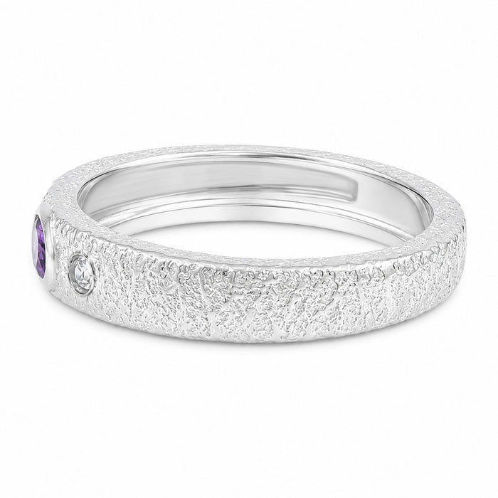 A textured silver band ring featuring a small purple oval gemstone on the left and a small round clear stone, shown on a plain white background.