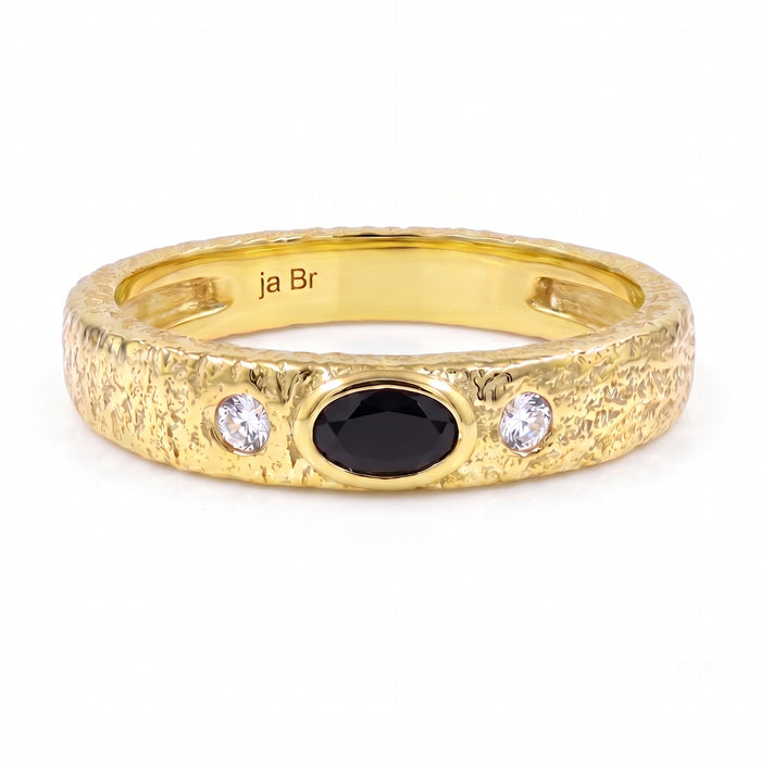 A textured yellow gold ring featuring a central oval black onyx and two round clear swarovski crystal on the shoulders, shown on a white background.