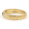 A textured yellow gold ring with a black onyx oval gemstone on one side and a small clear round gemstone on the other, shown on a white background.
