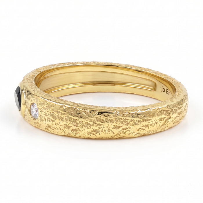 A textured yellow gold ring with a black onyx oval gemstone on one side and a small clear round gemstone on the other, shown on a white background.
