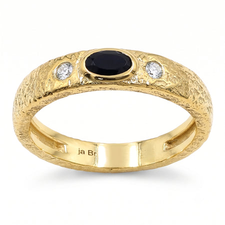 A textured yellow gold ring featuring a central oval black onyx and two round clear swarovski crystal on the shoulders, shown on a white background.