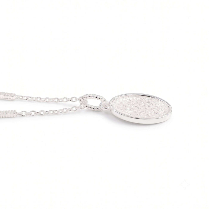 A silver oval pendant necklace with a textured, hammered finish inside a polished bezel setting, suspended from a delicate link chain against a plain white background.