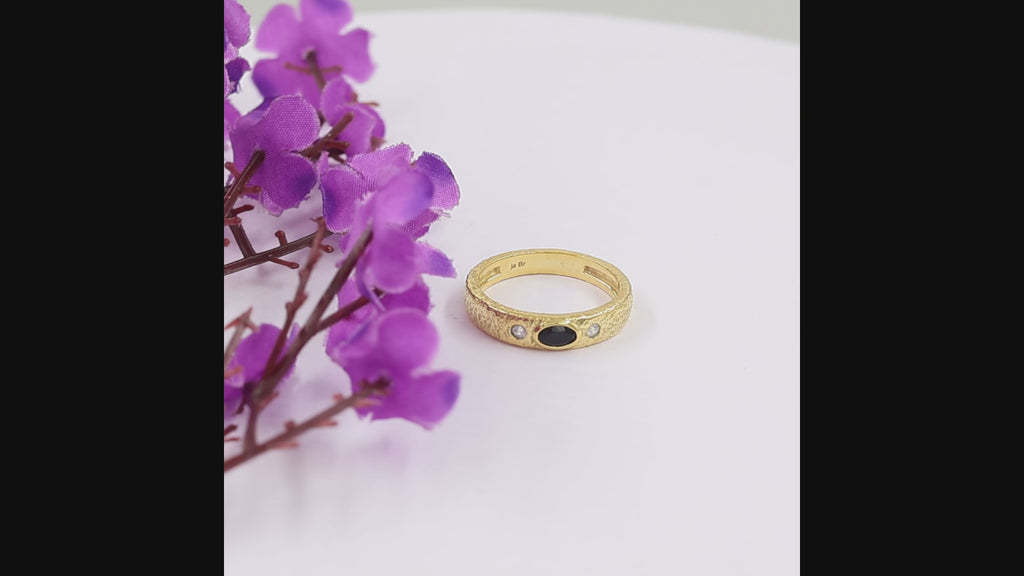 A textured yellow gold ring featuring a central oval black onyx and two round clear swarovski crystal on the shoulders, shown on a white background.