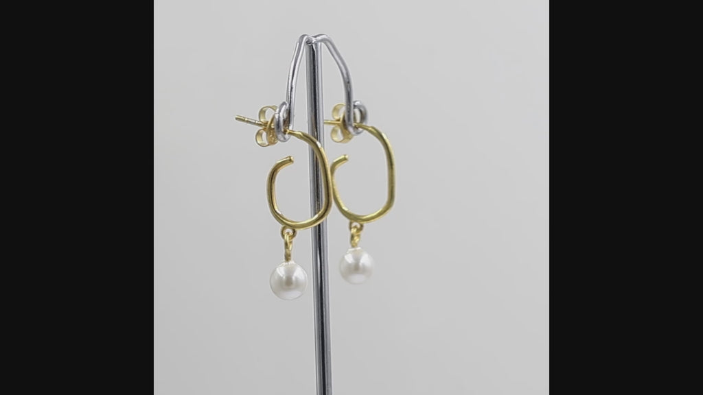 A pair of gold dangle earrings with a open hoop design and a freshwater pearl hanging from each earring, shown against a plain white background.