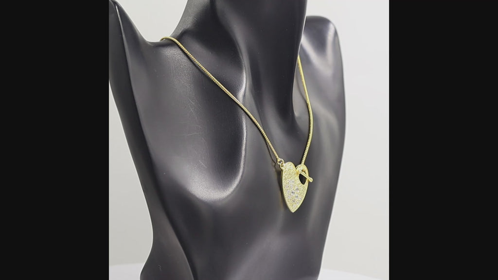A gold heart-shaped pendant necklace with a textured finish, featuring a row of clear swarovski crystal round-cut stones on the left side and a toggle clasp at the top right, suspended from a gold chain against a white background.