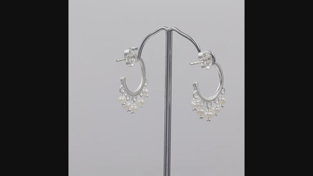A pair of silver hoop earrings with dangling pearl beads and small gold beads, shown on a plain white background.