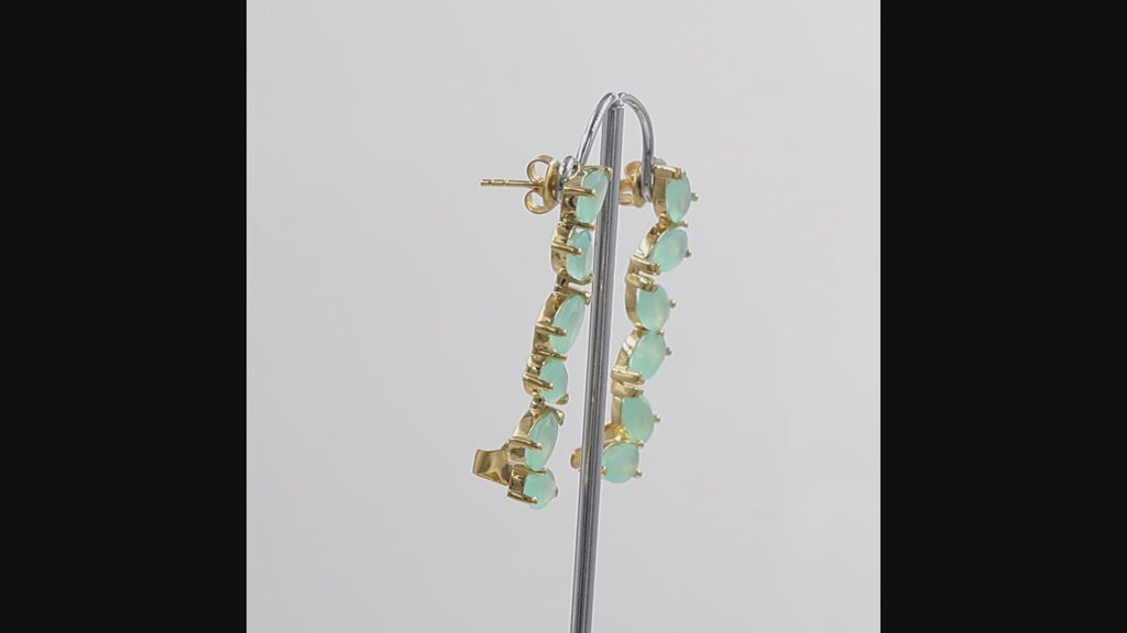 360 degree view of a pair of gold ear climber earrings featuring a vertical line of pear-shaped light aqua gemstones, shown  on a white background.